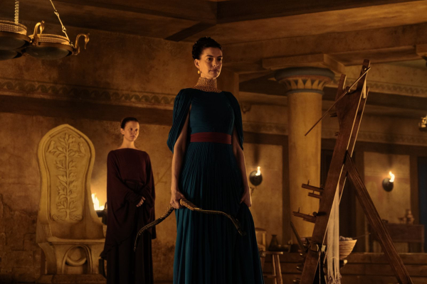 L to R Mia Goth is Melantho and Anne Hathaway is Penelope in THE ODYSSEY Penelope holds Odysseus's arrow in one hand.