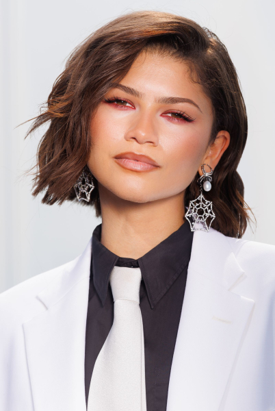 Zendaya wearing a white suit and tie black shirt and spiderweb earrings