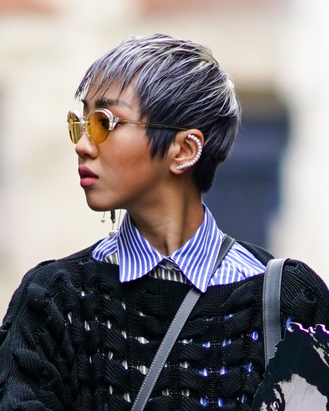 Woman wearing gray pixie cut sunglasses ear cuff and open knit black sweater over a blue striped shirt